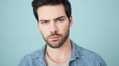 Şok olmuş genç adam kameraya bakıyor. Stüdyonun mavi arka planında tek başına duruyor.