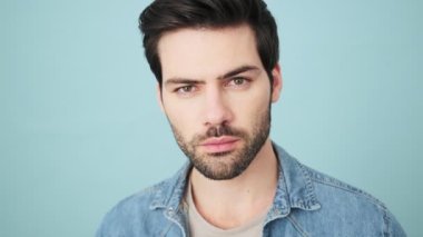 Gülümseyen genç bir adam kameraya bakıyor. Stüdyonun mavi arka planında tek başına duruyor.