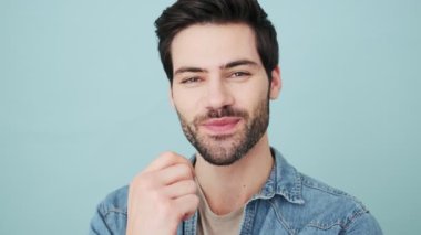 Mutlu genç bir adam kameraya poz veriyor. Stüdyoda mavi arka planda tek başına duruyor.