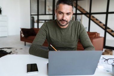 Modern bir ofiste çalışan, dizüstü bilgisayar kullanan, masada oturan, notlar alan yakışıklı, kendine güvenen genç bir iş adamı.