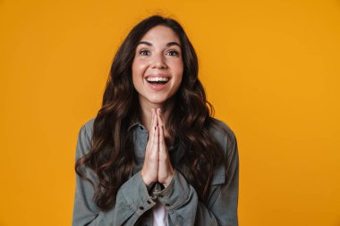 Neşeli güzel kız avuçlarıyla poz veriyor ve sarı arka planda izole bir şekilde gülümsüyor.