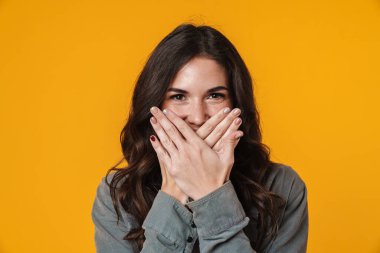 Mutlu güzel kız poz veriyor ve ağzını kapatıyor sarı arka planda izole edilmiş.