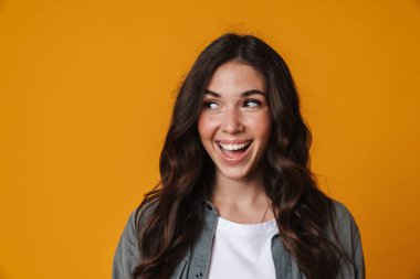 Neşeli güzel kız gülümsüyor ve sarı arka planda izole edilmiş bir kenara bakıyor.