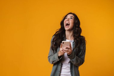 Sarı arka planda izole edilmiş cep telefonu kullanan güzel bir kız.