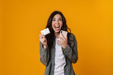 Sarı arka planda kredi kartı ve cep telefonu tutan güzel bir kız.