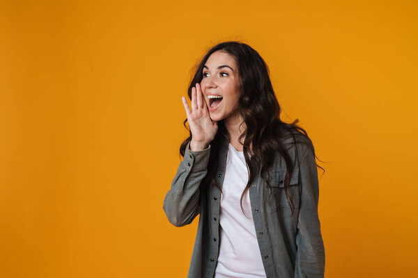 Радостная красивая девушка смотрит и кричит в сторону изолированы на желтом фоне