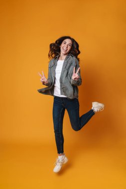 Heyecanlı güzel kız sarı arka planda tek başına atlarken barış işareti gösteriyor.