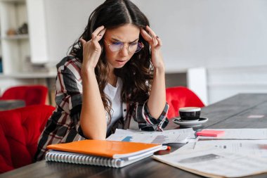 Ofiste belgelerle çalışan kafası karışmış genç bir kadın.