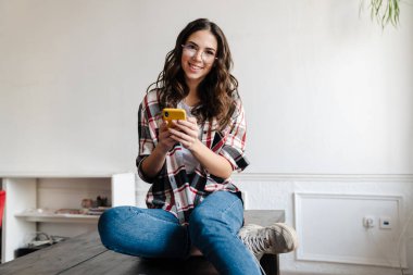 İçerideki masada otururken cep telefonu kullanan mutlu, güzel esmer kadın.