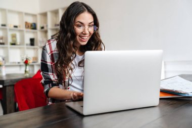 Gülümseyen ve kafede otururken dizüstü bilgisayarla çalışan mutlu bir kadın.