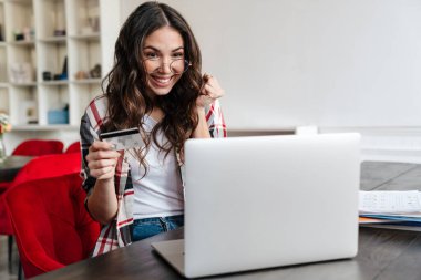 Kredi kartı tutan ve kafede dizüstü bilgisayarla çalışan mutlu bir kadın.