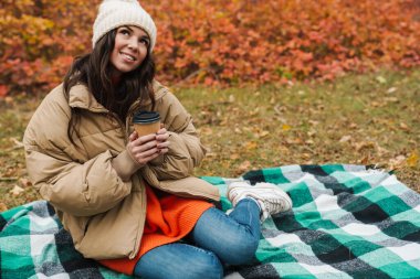 Mutlu kadın sonbahar parkında kahve içiyor.