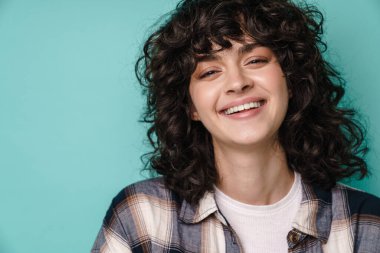 Neşeli, güzel kıvırcık kız gülümseyen ve mavi arka planda izole edilmiş kameraya bakan.