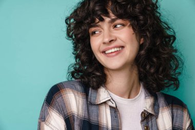 Neşeli, güzel, kıvırcık kız gülümseyen ve mavi arka planda tek başına bir kenara bakan.