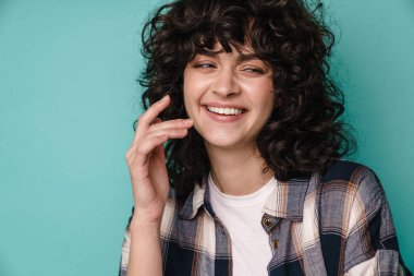 Neşeli, güzel, kıvırcık kız gülümseyen ve mavi arka planda tek başına bir kenara bakan.