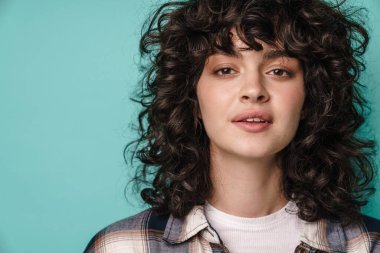 Kıvırcık esmer saçlı, mutlu bir kadın mavi arka planda tek başına duruyor.