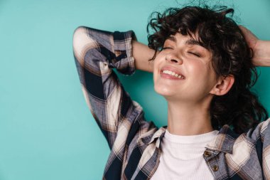 Kıvırcık esmer saçlı, mutlu bir kadın mavi arka planda tek başına duruyor.