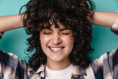 Kıvırcık esmer saçlı, mutlu bir kadın mavi arka planda tek başına duruyor.