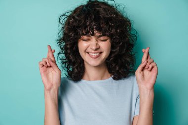 Neşeli kıvırcık kız şans dilemek için mavi arka planda poz veriyor.