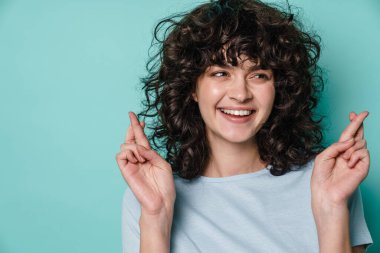 Neşeli kıvırcık kız şans dilemek için mavi arka planda poz veriyor.