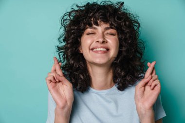 Neşeli kıvırcık kız şans dilemek için mavi arka planda poz veriyor.