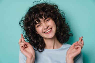 Neşeli kıvırcık kız şans dilemek için mavi arka planda poz veriyor.