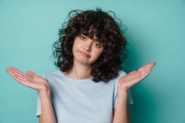 Mutsuz, güzel, kıvırcık kız. Mavi arka plan üzerinde poz veren ve alan tutan.