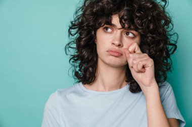 Beyaz mutsuz kıvırcık kız mavi arka planda izole edilmiş kameraya poz veriyor ve ağlıyor.