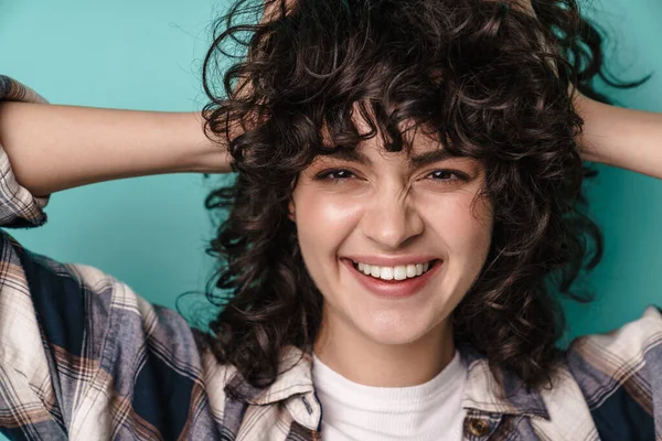 Kıvırcık esmer saçlı, mutlu bir kadın mavi arka planda tek başına duruyor.