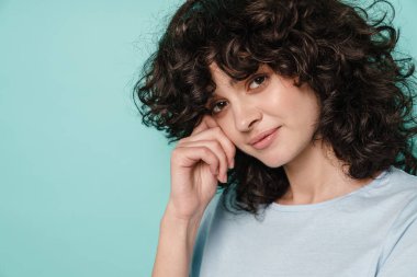 Beyaz, kıvırcık kız mavi arka planda yalnız poz veriyor ve kameraya bakıyor.