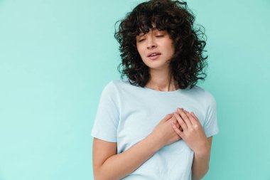 Beyaz, güzel, kıvırcık kız, mavi arka planda tek başına göğsünün üstünde el ele tutuşuyor.