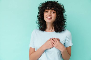 Beyaz, güzel, kıvırcık kız, mavi arka planda tek başına göğsünün üstünde el ele tutuşuyor.