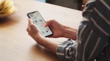 Dövmeli genç bir kadının kırpılmış görüntüsü akıllı telefonunu evde masada otururken kullanıyor.