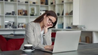 Gözlüklü genç bir iş kadını dairelerde dizüstü bilgisayarıyla çalışıyor.