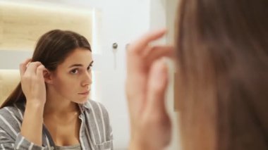 Çekici genç bir kadın dairelerdeki aynaya bakıyor.