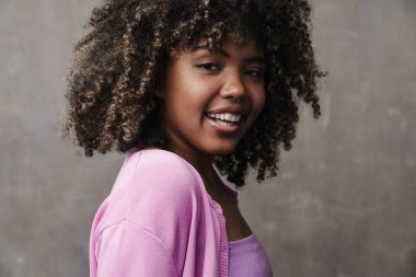 Neşeli Afro-Amerikalı kadın gri duvarın üzerinden izole edilmiş kameraya poz veriyor ve gülümsüyor.