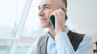 Ciddi bir yetişkin adam akıllı telefonuyla konuşuyor. Halka açık alanda oturuyor.