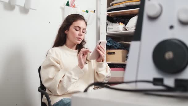 Een Positieve Jonge Vrouw Naaister Met Behulp Van Haar Smartphone — Stockvideo