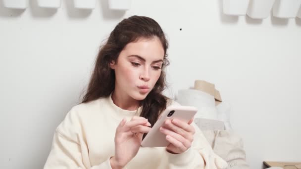 Een Aantrekkelijke Jonge Vrouw Naaister Met Behulp Van Haar Smartphone — Stockvideo