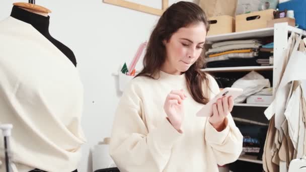 Una Joven Costurera Feliz Está Utilizando Teléfono Inteligente Mientras Hace — Vídeo de stock