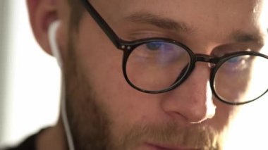 Gözlüklü bir gencin yakın plan görüntüsü dizüstü bilgisayarıyla evde oturuyor.