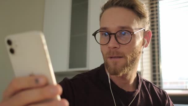 Atraktivní Mladý Muž Brýlemi Drátovými Sluchátky Používá Svůj Smartphone Sedí — Stock video