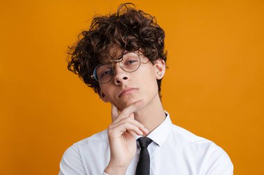 Sarı arka planda gözlük takan düşünceli genç bir öğrenci.