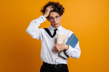 Üzgün, hayal kırıklığına uğramış, elinde kitap tutan üniversite öğrencisi sarı arka planda kendini yalnız hissediyor.