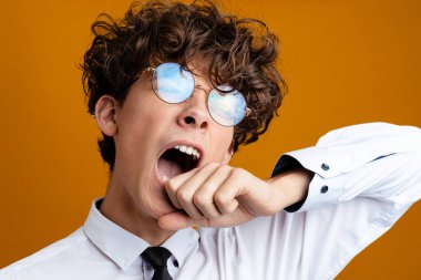 Üniforma giyen yorgun erkek öğrenci sarı arka planda izole edilmiş, esniyor.