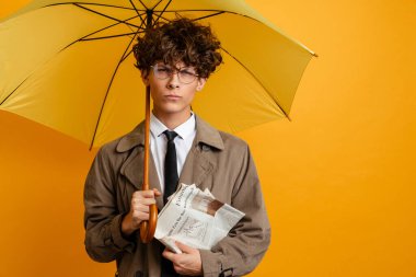 Sarı arka planda şemsiyesi olan şık genç bir adam elinde gazete tutuyor.