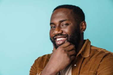 Neşeli Afrikalı Amerikalı adam gülümsüyor ve mavi arka planda izole edilmiş kameraya bakıyor.