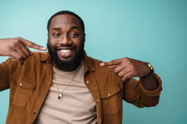 Mavi arka planda izole edilmiş, kendini işaret eden mutlu, heyecanlı bir Afrikalı adama yaklaş.