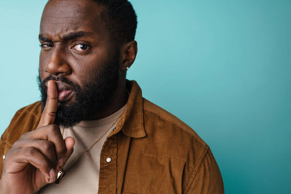 Displeased african american man showing silence gesture at camera isolated over blue background