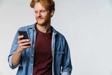 Beyaz arka planda izole edilmiş cep telefonu kullanırken gülümseyen Kafkasyalı kızıl adam.